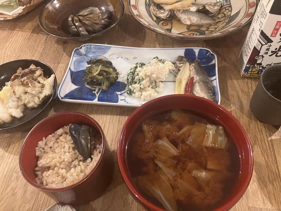 The image features a traditional Japanese meal with a variety of dishes. It includes a bowl of rice, a bowl of miso soup with cabbage, and several small plates of side dishes, including tempura and vegetables. There are also small fish and a