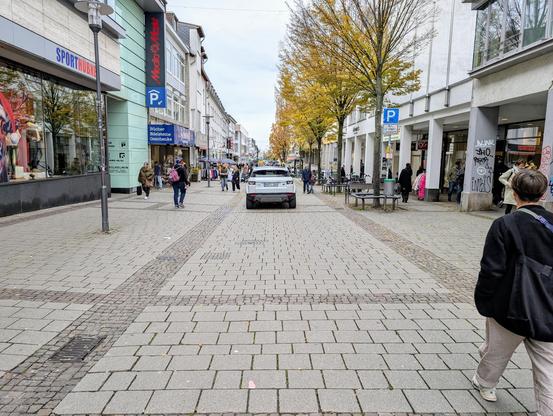 Fußgängerzone in Darmstadt, wo ein weißer Range Rover aus Heilbronn von oben bis unten durch fährt. Links und rechts Läden und Menschen