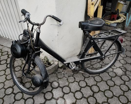 Das Bild zeigt eine Velo Solex auch nur Solex genannt. Sie steht an der Ecke einer Garage die offen ist.