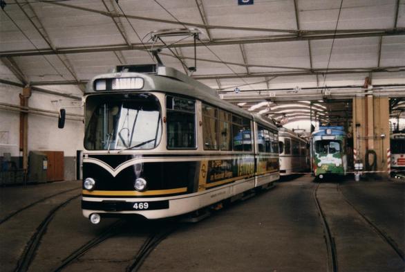 Foto im Querformat. In einer Halle mit mehreren Straßenbahnen steht eine im Vordergrund. Typisches DüWAG-Design, Wagennummer 469, mit Werbung für einen Opel-Händler. Die Zielanzeige ist rot auf weiß und lautet „Sonderfahrt“.