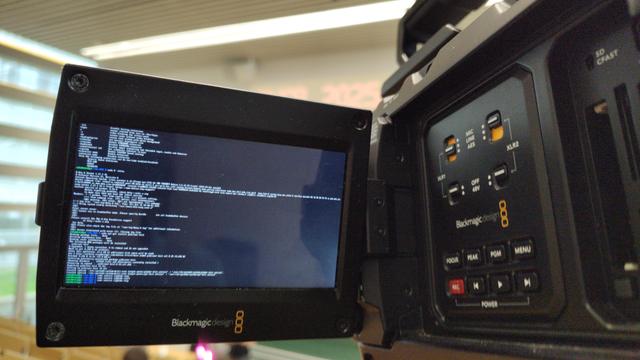 Preview display of a Blackmagic URSA camera showing a linux terminal with tiny text.