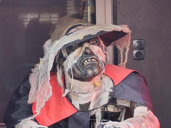 Zombieartige Gestalt mit Hut und rotem Kragen an der Eintrittskassa.