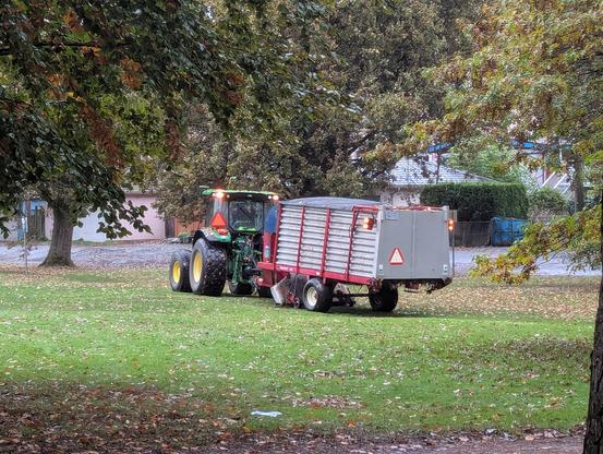 a tractor with a leaf removal trailer on grass in a park