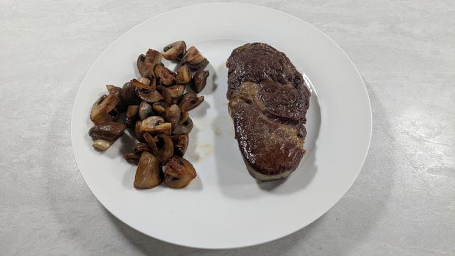 A white plate with a steak and fried mushrooms