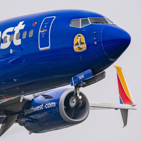 Cockpit end of a landing Southwest 737, showing a decal that honors Charles E. Taylor. The nose gear, port engine, and port wingtip/winglet are all visible.