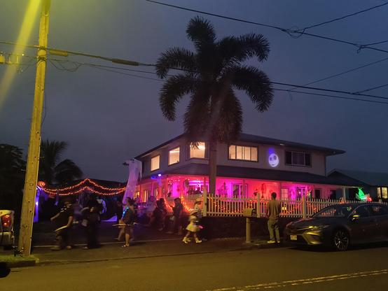 A house lit up in pink for Halloween, with people coming and going.