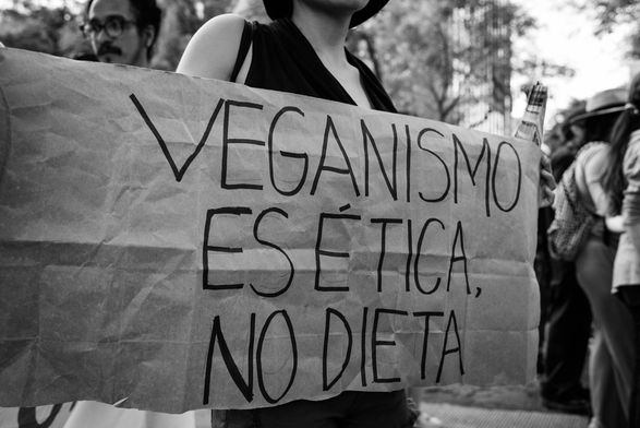 Fotografía en blanco y negro en una protesta contra el especismo en Ciudad de México. Une compa sostiene un cartel que a la letra dice: VEGANISMO ES ÉTICA, NO DIETA. © Sofía Dumat|CLAMOR DE LIBERTAD
