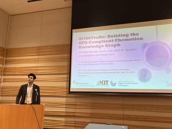 Ebrahim presenting his talk "AI4DiTraRe: Building the BFO-Compliant Chemotion
Knowledge Graph" at the Sci-K 2025 Workshop at ISWC 2025 in Nara, Japan. Ebrahim is rearing a grey jacket over a white shirt, standing left of the projected presentation slides, showing the title slide of his talk.