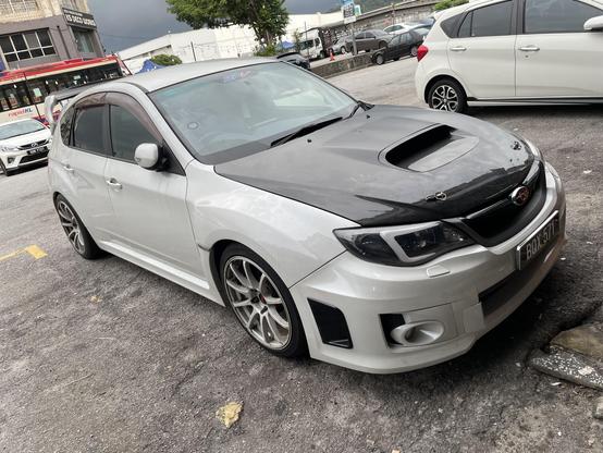 A white hatchback Subaru Impreza that has been modified
