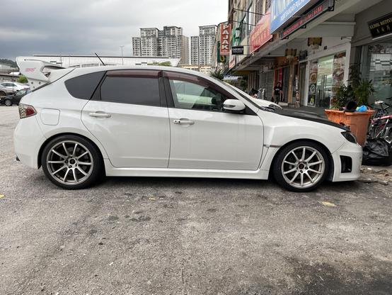 A white hatchback Subaru Impreza that has been modified