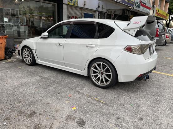 A white hatchback Subaru Impreza that has been modified