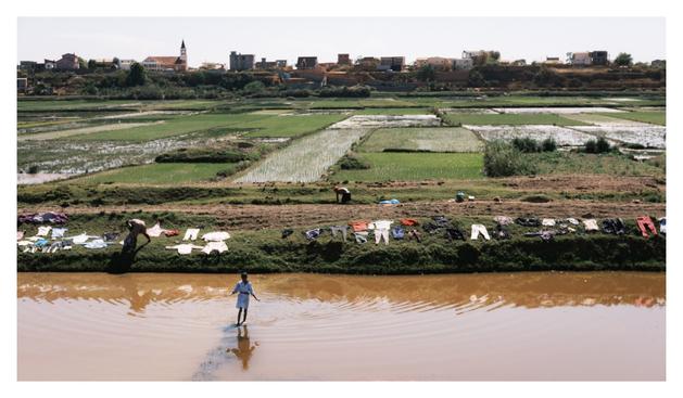 des rizières, du linge qui sèche au soleil, et un enfant qui traverse un canal d’irrigation à gué.