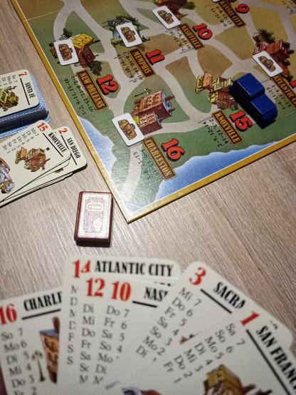 Meine Handkarten mit US-amerikanischen Stadtenamen und Wochentagen, die anzeigen, wie viele Punkte es beim Besuch der Stadt an diesem Wochentag gibt. Dahinter das Spielbrett.