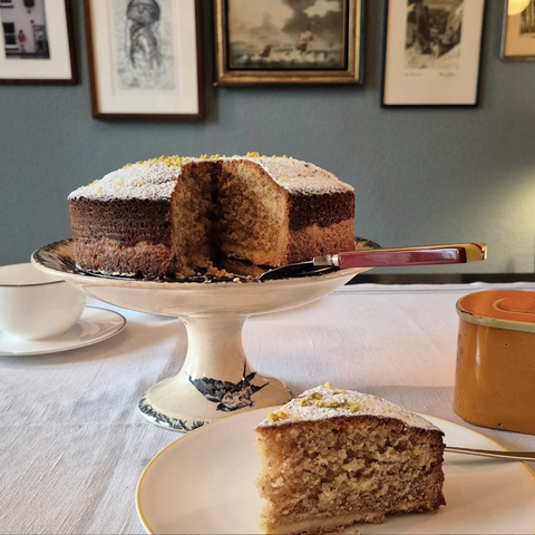 Ein Esszimmer. An der Wand Fotos mit Bilderrahmen. Auf dem Tisch die Herr Grün Tarte Florence mit Nüssen und einem krossen Mürbeteig. Obenauf Puderzucker.
