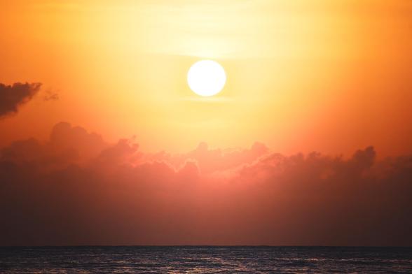 A sunsetting over the ocean, surrounded by orange and pink hues in the sky with soft clouds visible.
