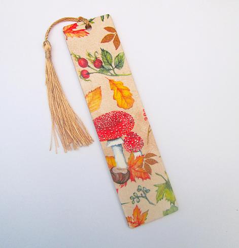 A wooden bookmark with a tassel, done with decoupage with the picture of autumn leaves, a toadstool and autumn berries, perfect for an autumn birthday gift.