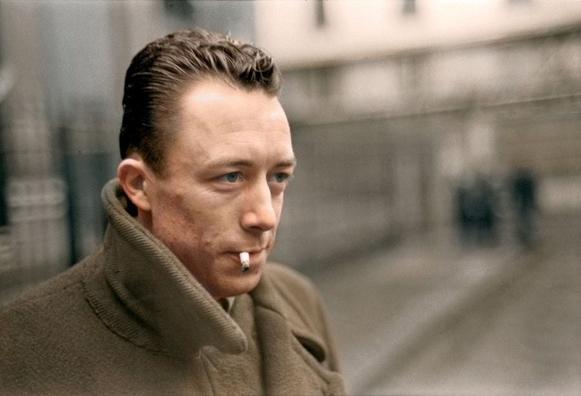 Albert Camus, regard perçant, marche en fumant une cigarette