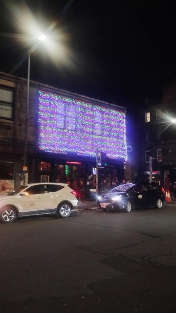 A two storey corner block at night, pub frontage on the ground floor, upper floor entirely covered by a curtain of colourful strings of lights hanging down