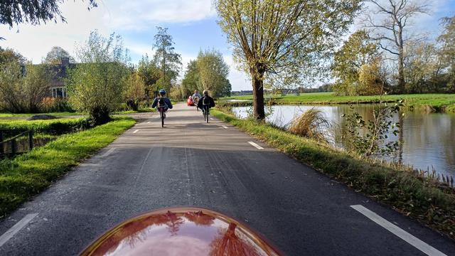 weggetje met links en rechts wat bomen, rechts een brede sloot, gefotografeerd over de rode neus van mijn Strada. voor mij rijden twee roeifietsen, daarvoor een Flevobike met wit stoeltje, en daarvoor een rode Quatrevelo