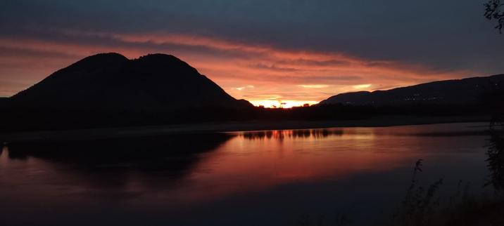 Sunrise casting pink on low clouds behind mountain silhouettes and mirrored on a still river.