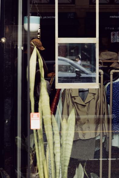 A reflection in a storefront mirror frames a woman walking across the street.