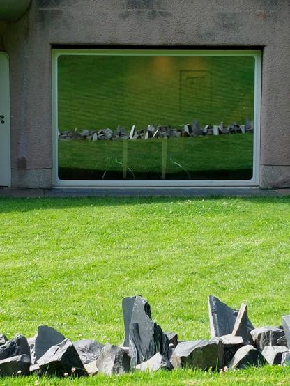 Im Fenster der historischen Villa "Waldfrieden" im Skulpturenpark in Wuppertal spiegelt sich die Arbeit "Basalt Slate" des LandArt-Künstlers Richard Long. Das 2015 entstandene Werk, eine gerade Linie aus schroffen, spitzen Basalt- und Schieferbrocken, liegt in der Wiese auf der Rückseite der Villa. 
Die kantige Skulptur bildet einen starken Kontrast zum organischen Gebäude, in dem es keine rechten Winkel gibt.