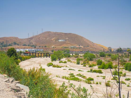 In the distance, a bridge crosses the dry riverbed of Santa Ana River, beneath a dry hill.
