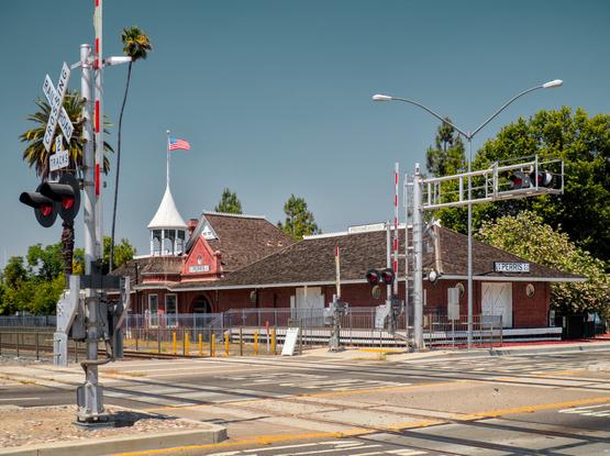 The (I suppose) Victorian style Perris train station seen from across the tracks. A crossbuck with warning lights is in the foreground.