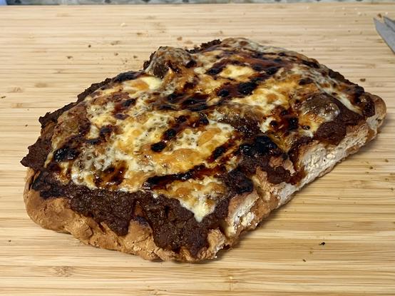 a slice of the same bread, trimmed and neatened into a rough rectangle, the top of which has been smothered with sauce and cheese and toasted under a grill