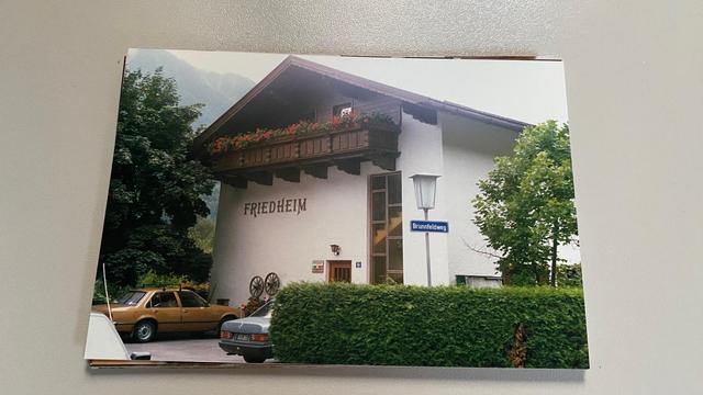 In Austria, we see a typical zimmer frei house to host several families or guests. 
It's a white building with a lot of wood: roof, balcony, doors... Two cars are parked in front of it. The Opel Record in light brown belonged to my dad.