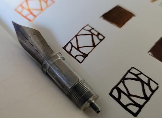 Titanium nib in clear housing. Background is mini doodles and small ink swatchs in brown.