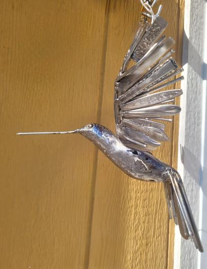 Monsieur Régent Chevalier 
Un colibri en acier est suspendu au soleil.  Le fond est jaune et blanc.

Il est composé à 100% d'acier revalorisé. On voit encore des clous et des manches d'ustensiles dans ses ailes.

De mémoire il mesurait autour de 10" de large