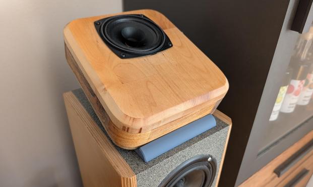 Ein kleiner Breitbandlautsprecher liegt auf einem Halter auf der Oberseite von großen Standlautsprechern.