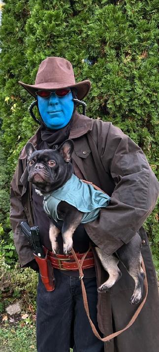A man dressed like a blue-skinned Star Wars character holds a French bulldog.