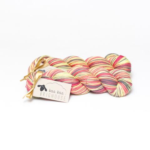 Picture shows two skeins of yarn, one behind the other, in shades of black, yellow, red and coral.