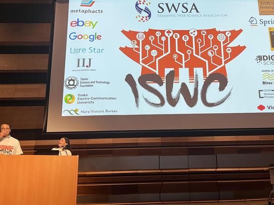 Kouji Kozali ( left) and Anna Lisa (right) on the big stage with the iswc2025 opening screen in the background