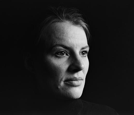 Halbschräges Porträt einer Frau mit schwarzen Haaren, die nach rechts blickt. Sie trägt ein dunkles Oberteil, der Hintergrund ist schwarz und lässt keine weiteren Details erkennen.