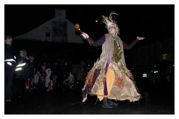 A witch mid dance surrounded by kids and in costumes on the street.