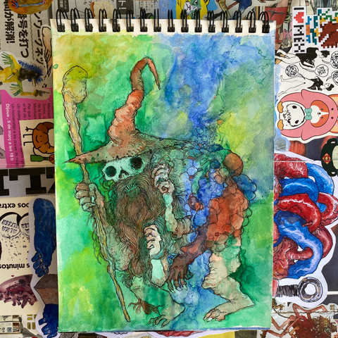 Cuaderno con una acuarela con manchones de muchos colores de un mago con cara de calavera.