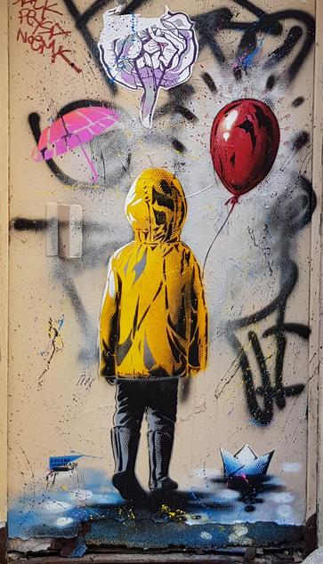 A kid in a yellow rain coat holding a red balloon, walking away from us on a wet blue floor.