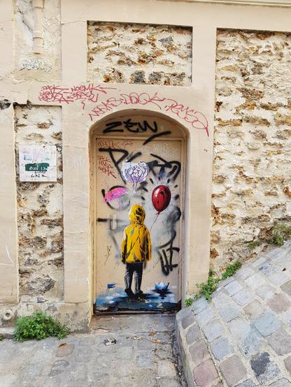 A kid in a yellow rain coat holding a red balloon, walking away from us on a wet blue floor. In an archway in the middle of brick wall and paved street in Montmartre.
