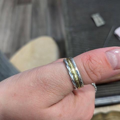 Two silver and one brass stacking ring with different textures, worn on a thumb