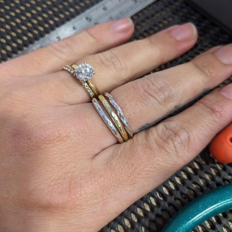 Two silver and one brass stacking ring on a middle finger. The ring finger also has rings.