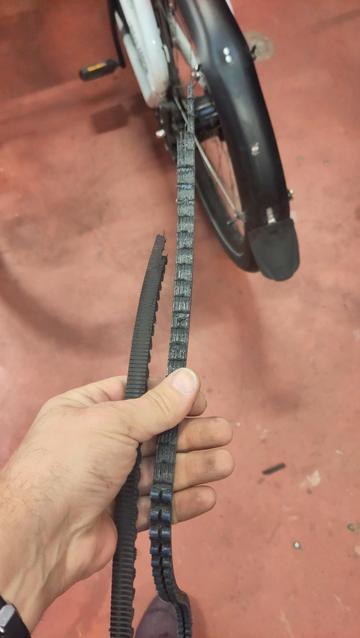 Courroie de transmission de vélo électrique cassée en deux. En arrière plan, l'arrière d'un vélocargo blanc