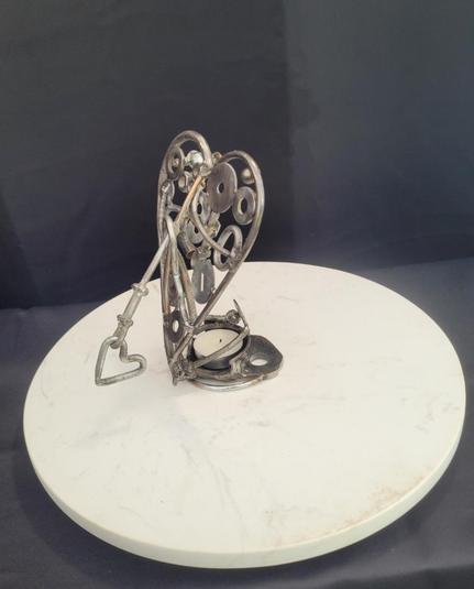 Chandelier coeur percé 

Un chandelier pour 1 seul lampion en forme de coeur transpercé par une flèche. L'ensemble est fait de rebut en acier: boulon, washer, chaîne de scie, vis, etc