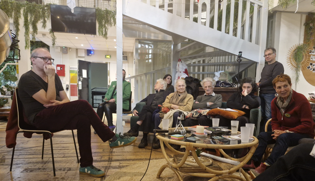 David Cormand, à gauche de l'image, habillé en oir, assis sur une chaise, écoute l'un des participants à la soirée qui lu pose une question.