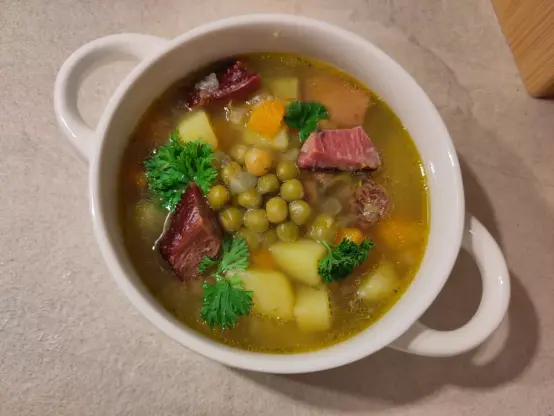 Eine Suppentasse gefüllt mit einer kleinen Portion des Erbseneintopfs. Die Gemüseeinlage ist klar zu sehen in der Suppe. Es ist kein "Gemüsematsch" entstanden. Außerdem sind die Stücke vom Kassler und etwas frische Petersilie zu sehen.