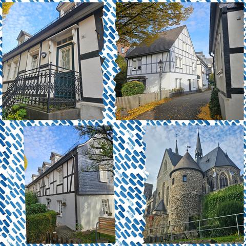Vier Fotos zeigen verschiedene Gebäude in einer historischen Altstadt. Das erste Bild zeigt einen Hauseingang mit einer schwarzen, kunstvoll gestalteten Metallbrüstung und einer weißen Tür mit Glasfenster. Das zweite Bild zeigt ein weißes Fachwerkhaus mit einem schrägen Dach, davor ein kleiner Garten mit einem Holzzaun und herbstlich gefärbten Blättern auf dem Gehweg. Das dritte Bild zeigt ein langgestrecktes Fachwerkhaus mit weißen Wänden und dunklen Holzbalken, davor ein kleiner Garten mit einer Bank. Das vierte Bild zeigt eine große, steinerne Kirche mit runden Türmen, spitzen Dächern und einem hohen Kirchturm, umgeben von einer grünen Hecke und einem Zaun.