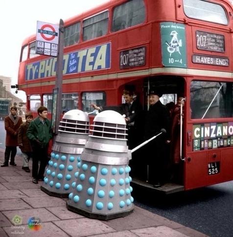 Two Dr Who Daleks trying to board an old fashioned double decker London bus, with a TYPHOO TEA advertisement on the side