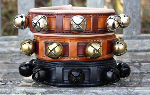 3 leather collars, stacked. Each is made from straps of leather woven together with sleigh bells attached, all in different colorways. Top is shades of brown with silver bells; middle is shades of brown with brass bells; bottom is solid black with black bells
